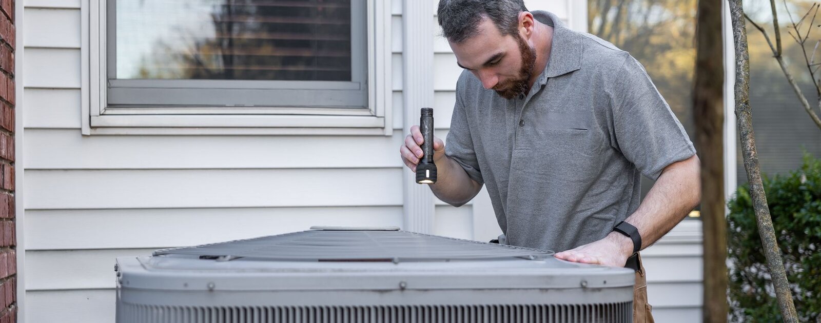 HVAC technician inspecting an outdoor AC condenser during a repair call in Tulsa